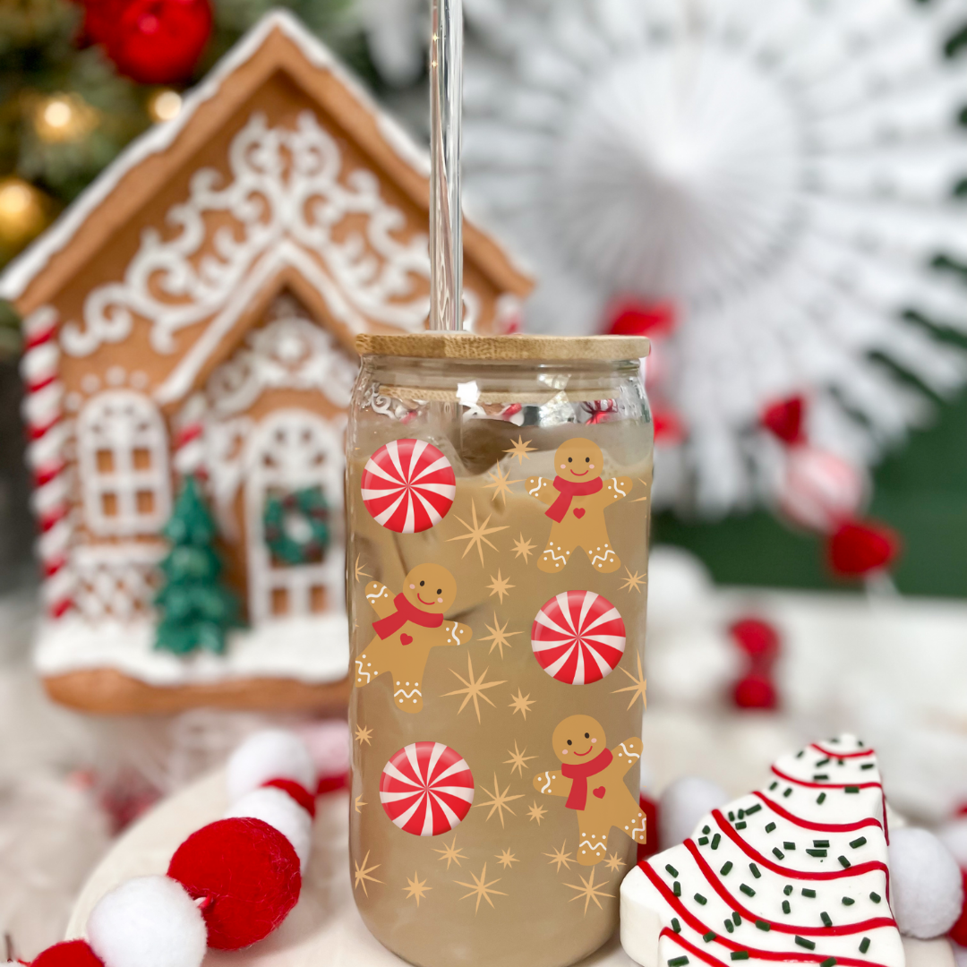 Verre transparent 16 oz avec couvercle de bambou et paille de verre au thème de Noël, décoré de bonbons rouge et blanc et de pains d'épices, avec en arrière plan un décor de Noël dont une maisonnette en gingembre.
