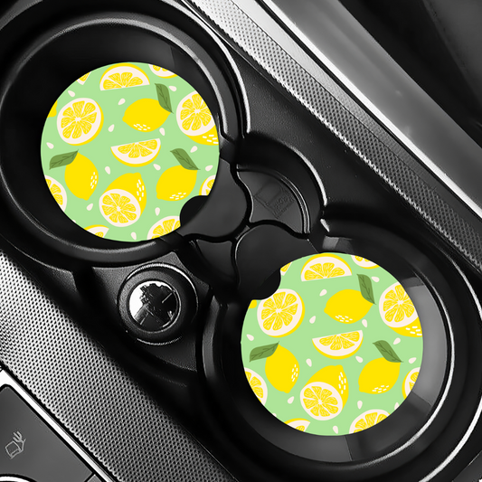 Duo de sous-verres pour auto motif citrons jaunes installés dans les porte-gobelets noirs d'une voiture.