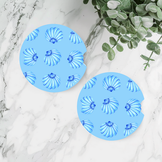 Duo de sous-verres pour voiture motif coquillages bleus et blancs sur fond de sable avec étoile de mer.