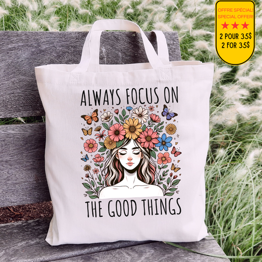 Sac fourre-tout en coton de couleur naturel de 15 x 16 pouces avec un design boho d'une femme entourée de fleurs colorées et de papillons, accompagnée du texte “Always Focus on the Good Things”.