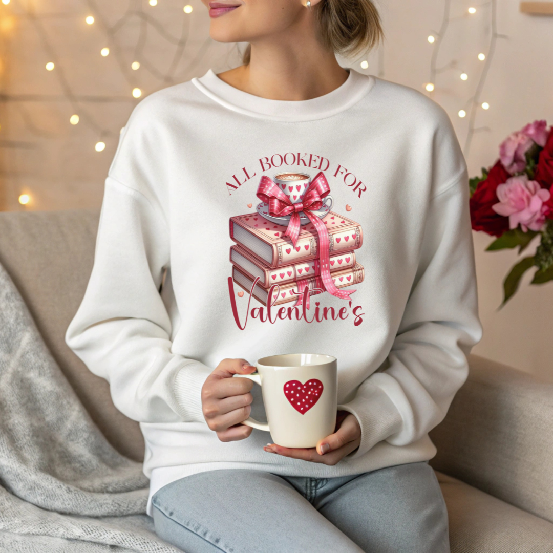 Mannequin portant un sweatshirt blanc avec un design  “All Booked for Valentine’s”, illustré par une pile de livres décorés de cœurs et une tasse de café, style romantique et cosy.