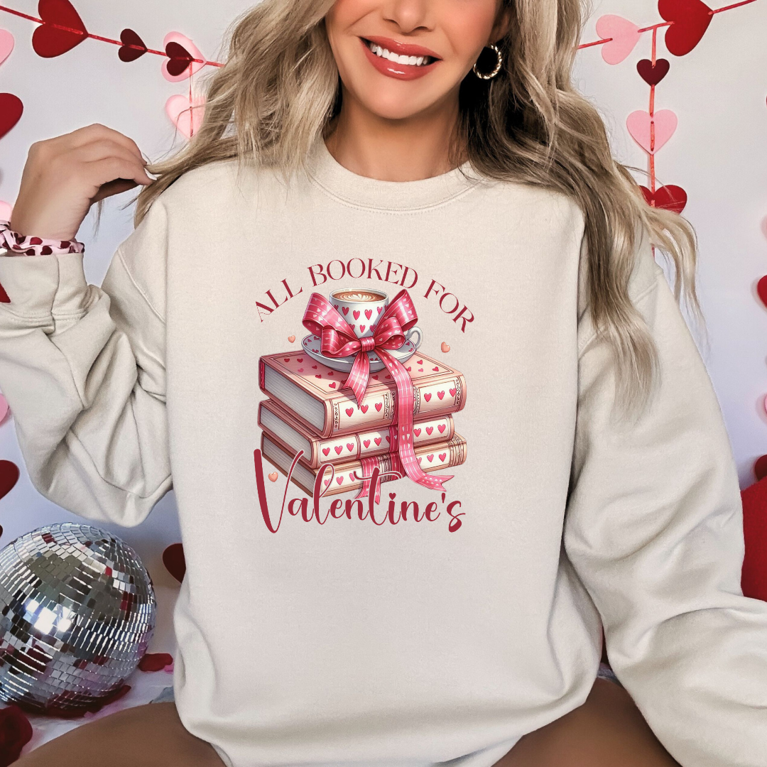Mannequin portant un sweatshirt sable avec un design  “All Booked for Valentine’s”, illustré par une pile de livres décorés de cœurs et une tasse de café, style romantique et cosy.