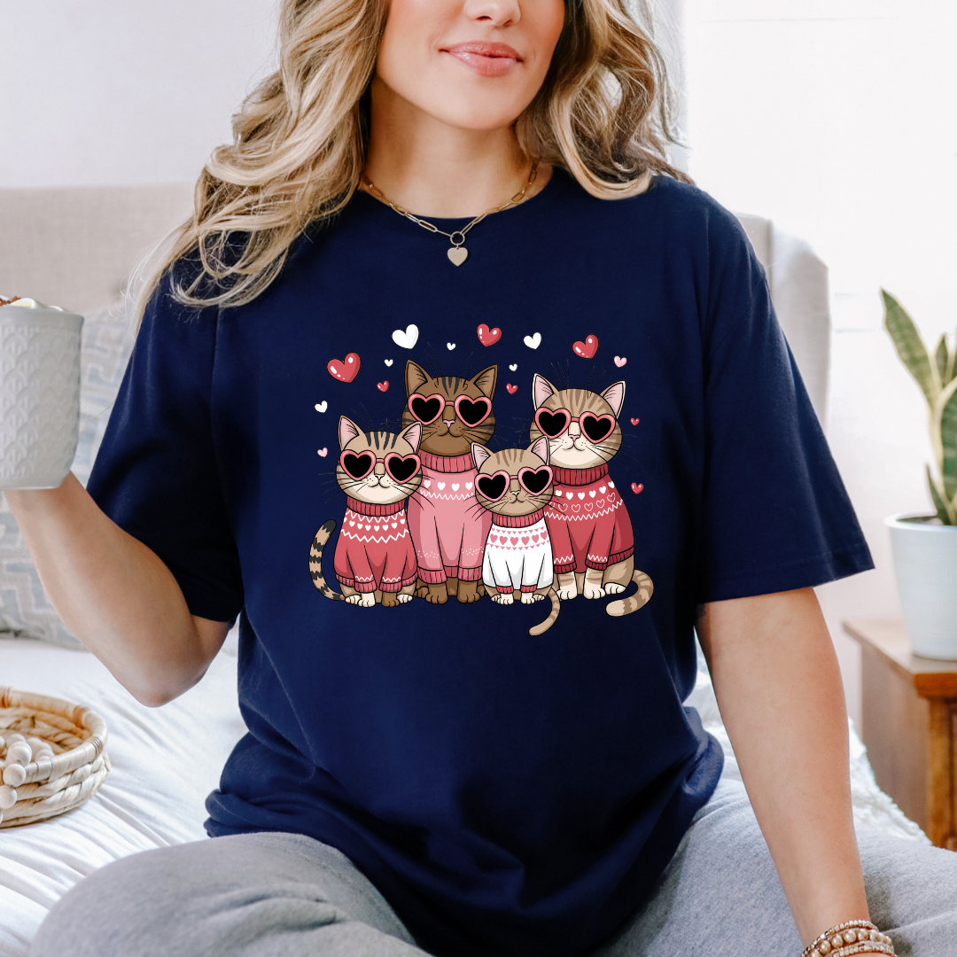 T-shirt bleu marine avec un motif de quatre chats portant des lunettes en forme de cœur et des pulls roses. Les chats sont entourés de petits cœurs roses.