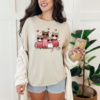 T-shirt sable avec un motif de quatre chats portant des lunettes en forme de cœur et des pulls roses. Les chats sont entourés de petits cœurs roses.