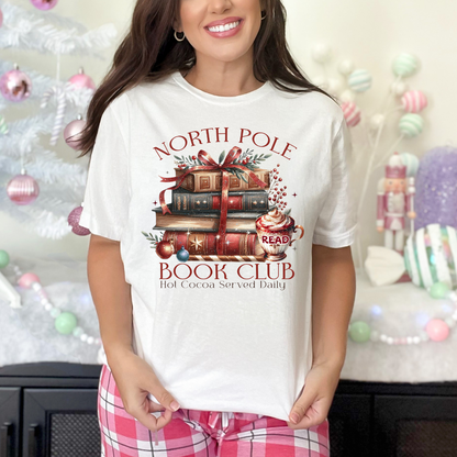 T-shirt Gildan Blanc avec un imprimé Livres de Noël empilés attachés d'un ruban rouge accompagnés d'une tasse de chocolat chaud. Ambiance cozy festive – parfait pour les fans de lecture !