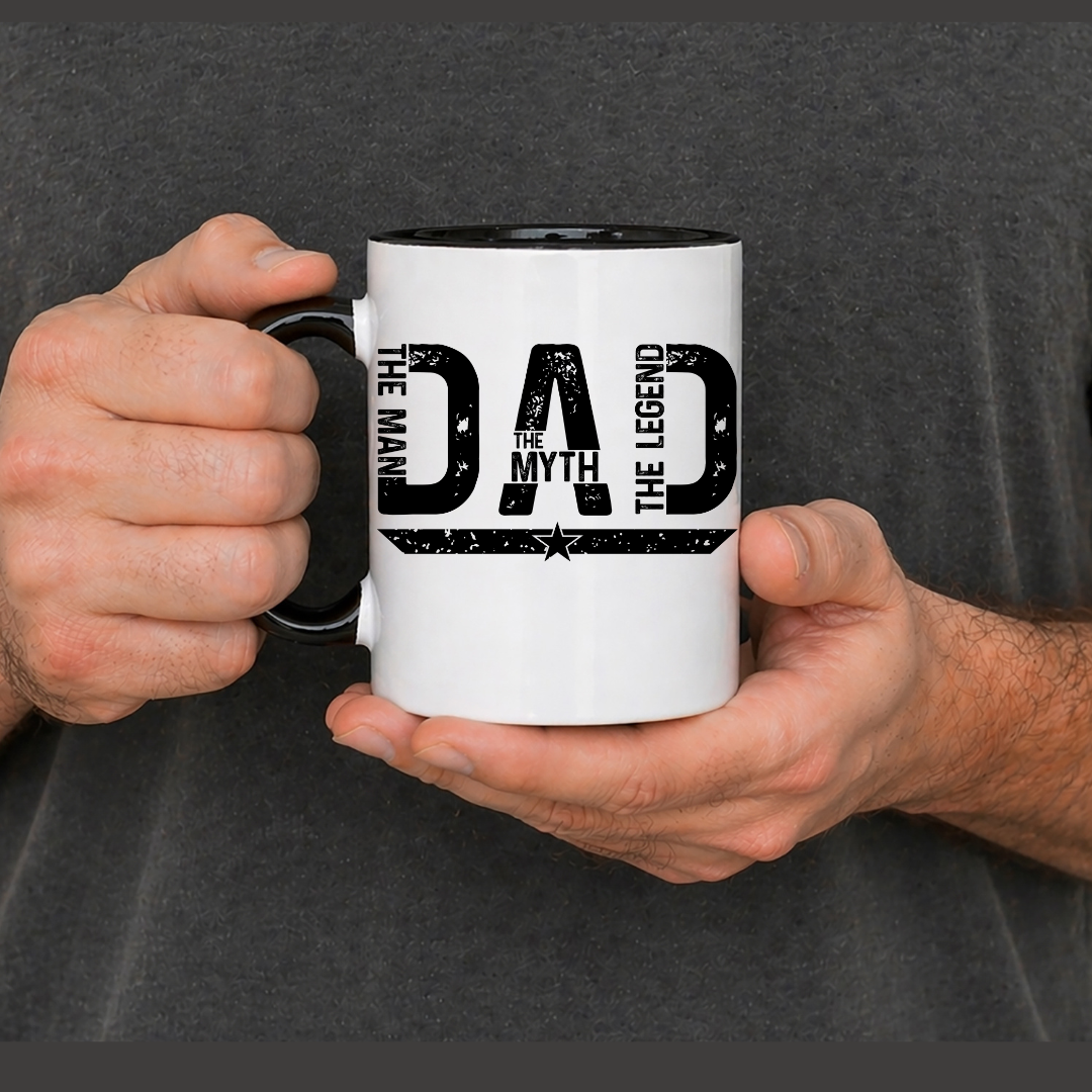 asse blanche en céramique de 15 oz tenue dans les mains, affichant le texte noir Dad The Man, The Myth, The Hero.