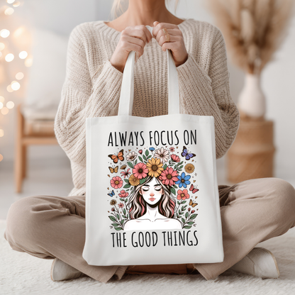 Sac fourre-tout en coton de couleur naturel de 15 x 16 pouces avec un design boho d'une femme entourée de fleurs colorées et de papillons, accompagnée du texte “Always Focus on the Good Things”.