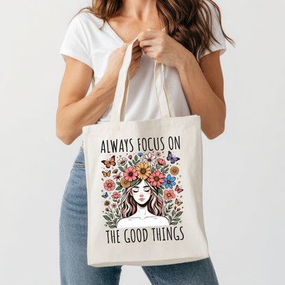 Sac fourre-tout en coton de couleur naturel de 15 x 16 pouces avec un design boho d'une femme entourée de fleurs colorées et de papillons, accompagnée du texte “Always Focus on the Good Things”.