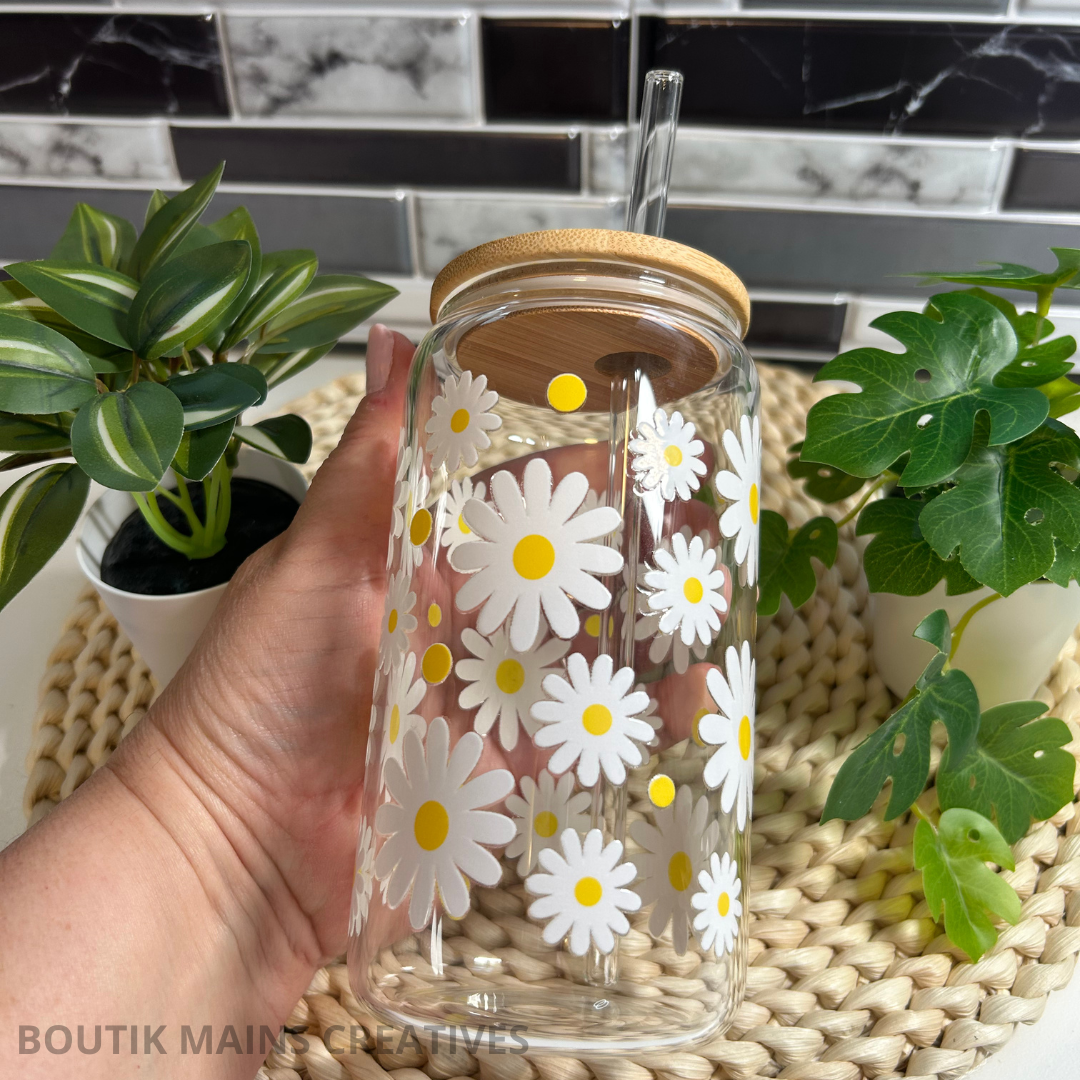 Verre à café glacé Libbey 16 oz transparent orné de marguerites blanches avec centres jaunes, incluant un couvercle en bambou et une paille en verre.