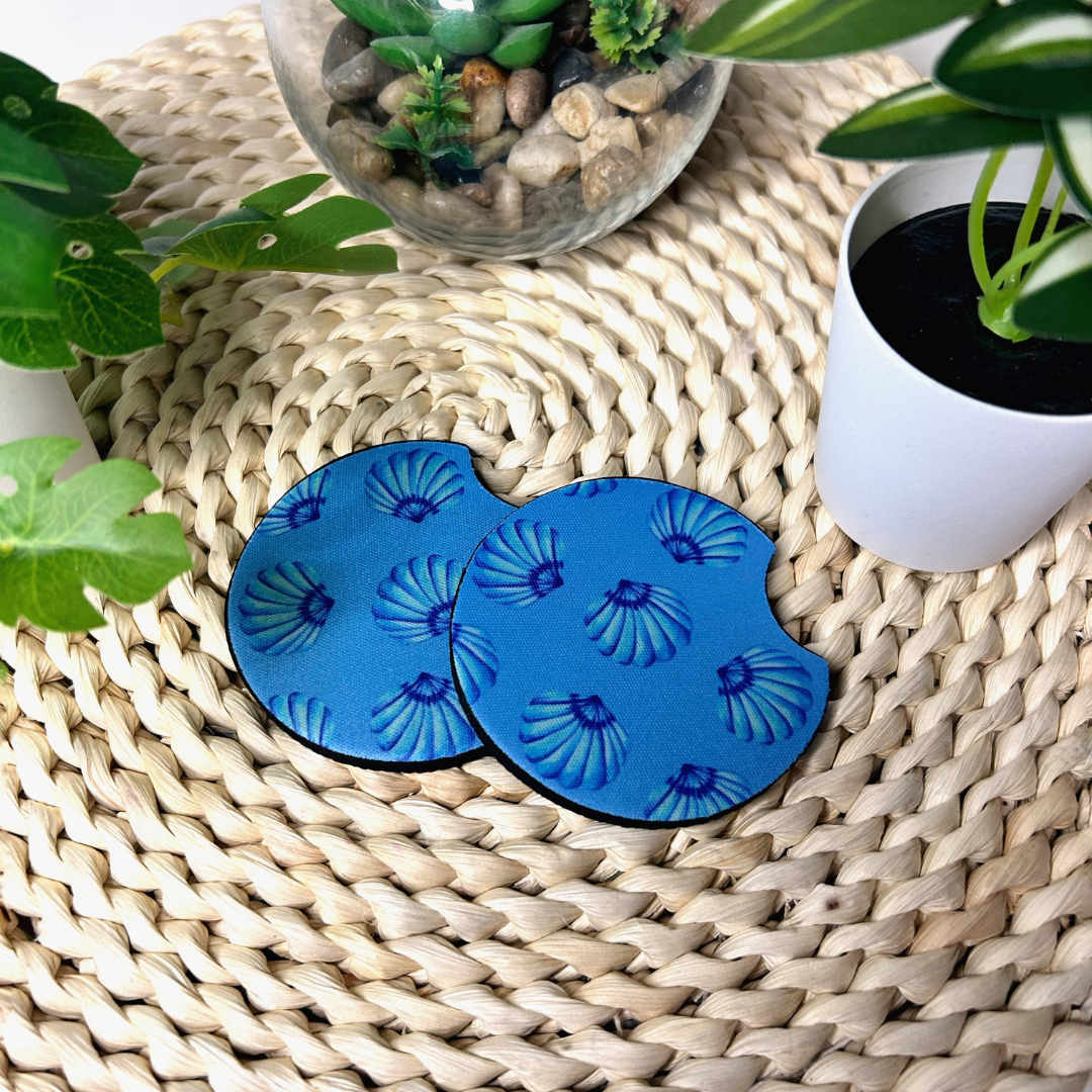 Duo de sous-verres pour voiture motif coquillages bleus et blancs sur fond de sable avec étoile de mer.