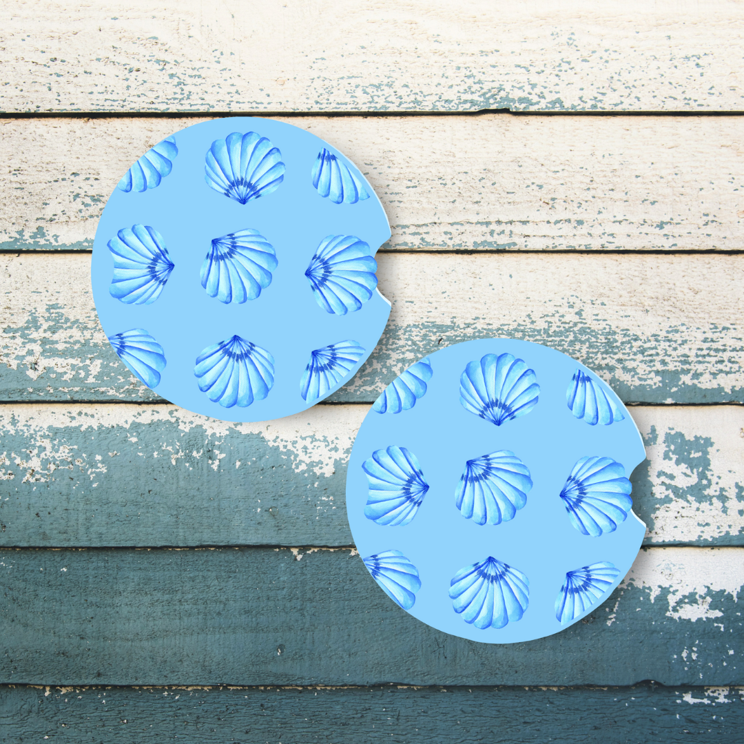 Duo de sous-verres pour voiture motif coquillages bleus et blancs sur fond de sable avec étoile de mer.