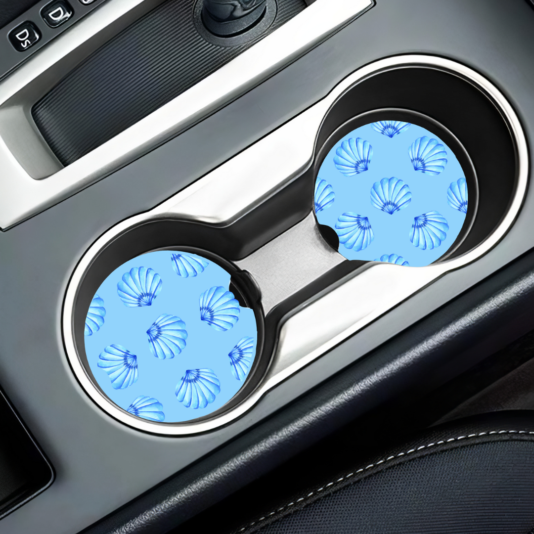 Sous-verres motif coquillages installés dans les porte-gobelets d'un véhicule pour une déco estivale.