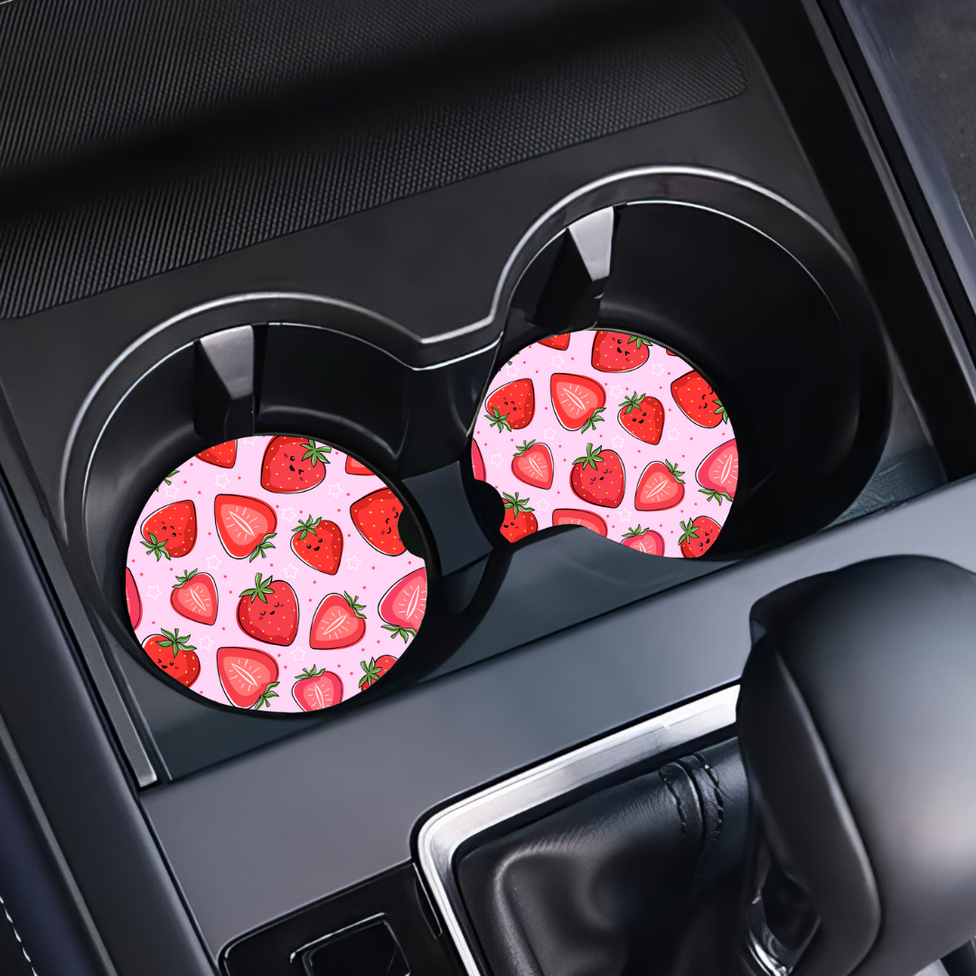 Sous-verres motif fraises installés dans les porte-gobelets noirs d'une voiture.