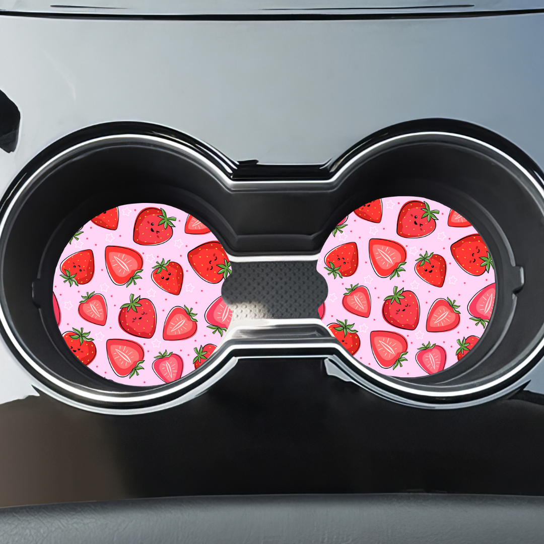 Sous-verres motif fraises installés dans les porte-gobelets noirs d'une voiture.