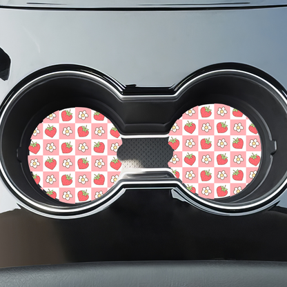 Sous-verres style rétro fraises et fleurs installés dans les porte-gobelets noirs d'une voiture.