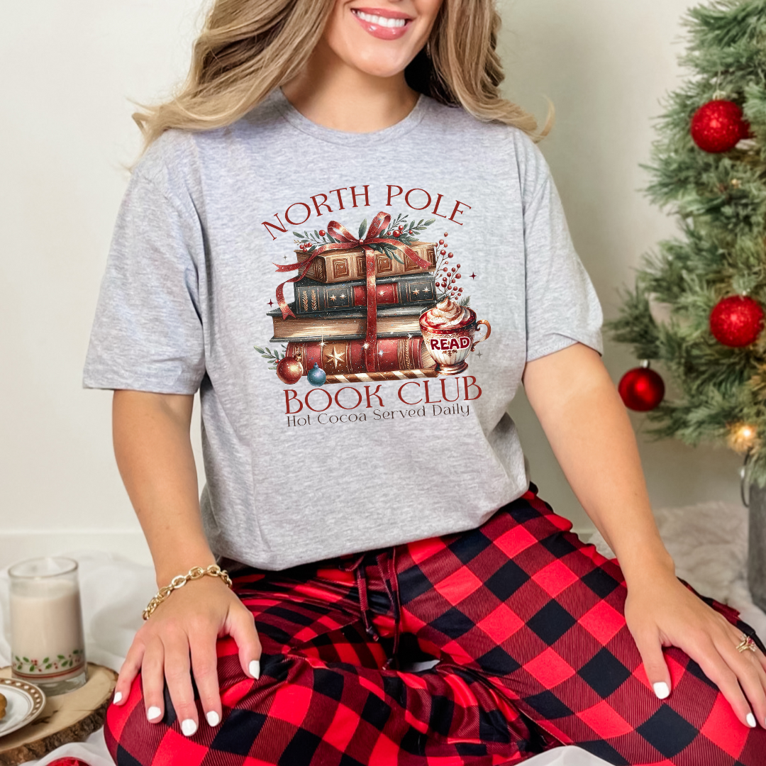 T-shirt Gildan gris athlétique avec un imprimé Livres de Noël empilés attachés d'un ruban rouge accompagnés d'une tasse de chocolat chaud. Ambiance cozy festive – parfait pour les fans de lecture !