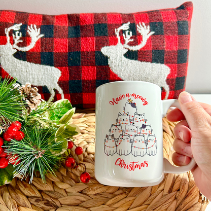 Tasse blanche de 15 oz avec un design "Meowy Christmas" montrant des chats empilés en forme de sapin de Noël avec des tuques rouges et des lumières colorées.