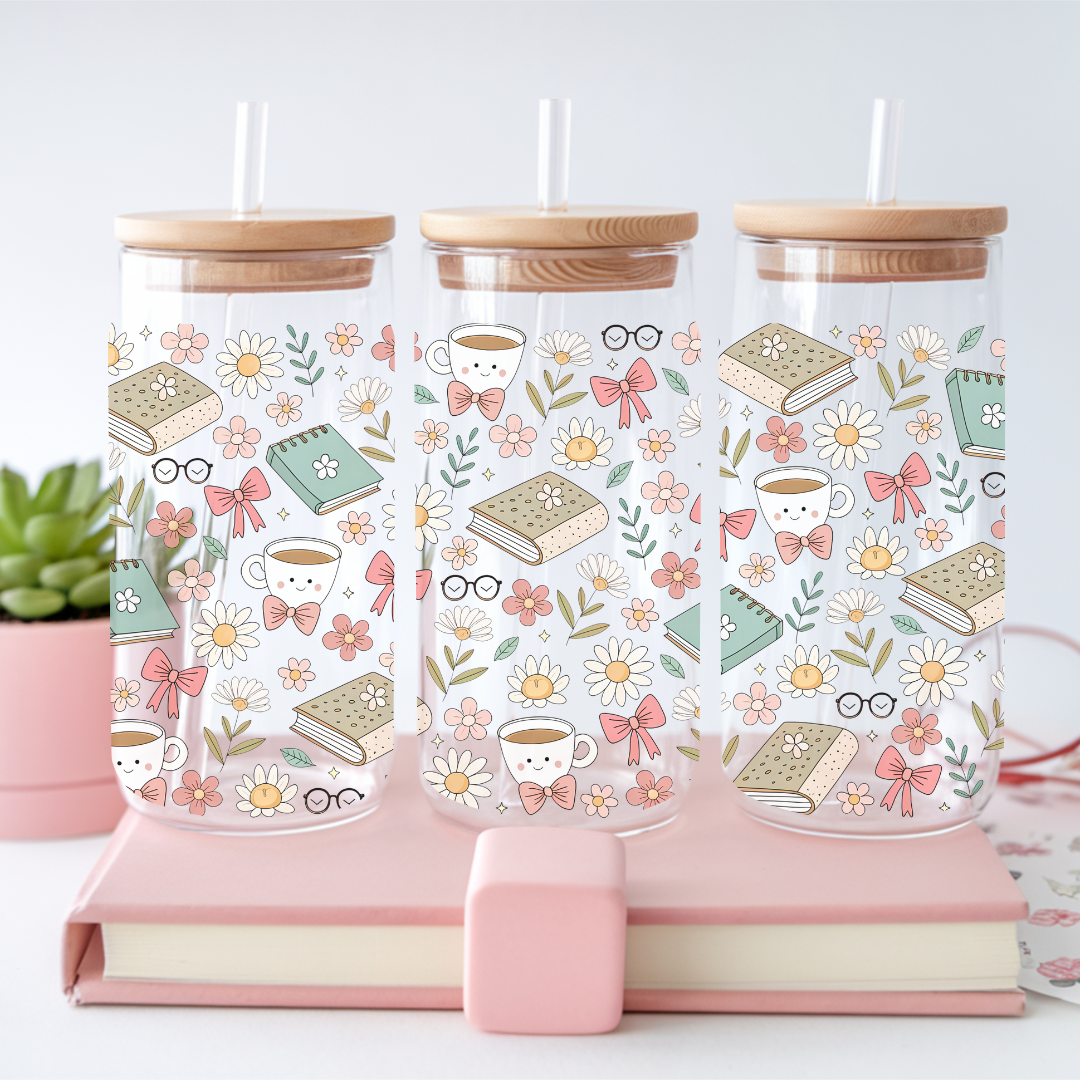 Verre à café glacé transparent de 16 oz orné de motifs de piles de livres et de tasses à café, avec couvercle en bambou et paille en verre, posé sur un dessous-de-verre en rotin