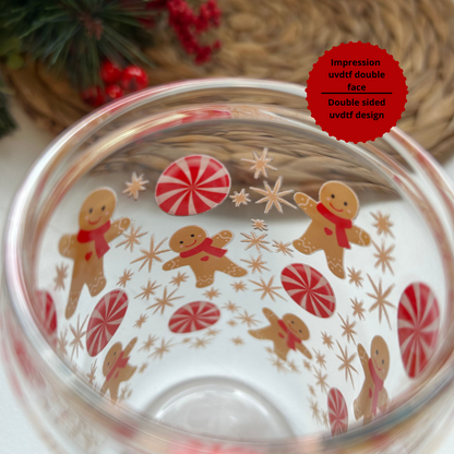 Verre transparent 16 oz au thème de Noël, décoré de bonbons rouge et blanc et de pains d'épices. Image démontrant la double impression du design visible à l'intérieur et extérieur du verre.